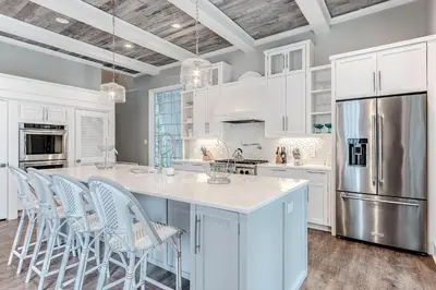 a kitchen with white cabinets and a large island with chairs at Carefree Cottage in Rosemary Beach