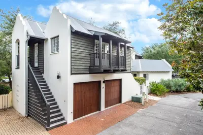 a white house with a brown door and a garage at Highland Carriage House in Rosemary Beach