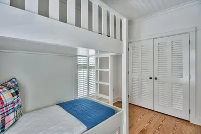 a white bedroom with a bunk bed and a staircase at McKenzie Cottage in Rosemary Beach