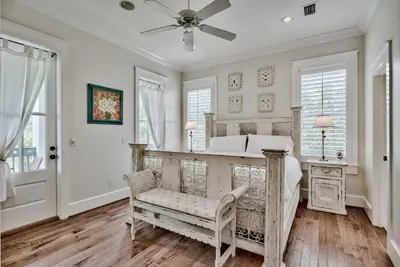 a bedroom with a bed and a chair and windows at Sylvia's Cottage in Rosemary Beach