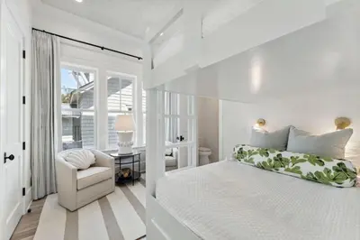 a white bedroom with a bed and a chair at Beach Bear Cottage in Watersound Beach