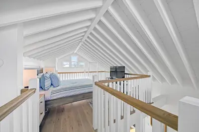 a white attic bedroom with a bed and stairs at Deauville Carriage House in Rosemary Beach
