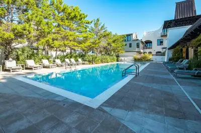 a swimming pool with chairs next to a building at Deauville Carriage House in Rosemary Beach