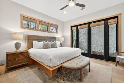 a bedroom with a bed and a chair and windows at Brighton Cottage in Rosemary Beach