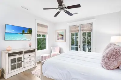 a white bedroom with a bed and a flat screen tv at Butterfly Cottage in Rosemary Beach