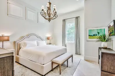 a white bedroom with a bed and a chandelier at Clare's Cottage in Seacrest