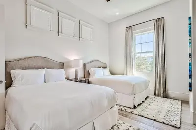 two beds in a white room with a window at Clare's Cottage in Seacrest
