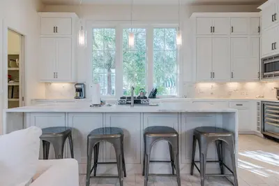 a kitchen with white cabinets and a counter with stools at Kidd Cottage in Rosemary Beach