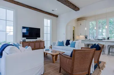 a living room with white couches and a kitchen at Kidd Cottage in Rosemary Beach