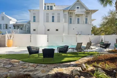 a yard with chairs and a pool in front of a house at Kingston Beach Club in Rosemary Beach