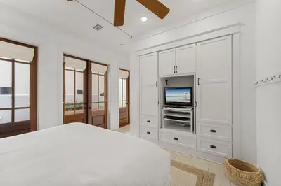a white bedroom with a bed and a tv at Hope Town Pearl Cottage in Rosemary Beach