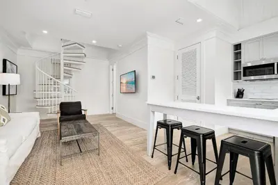 a white living room with a counter and stools at Bella Carriage House in Rosemary Beach