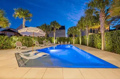 a pool with chairs and an umbrella and palm trees at 98 Sandy Shores Ct in Seacrest
