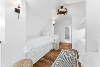 a white bedroom with two beds and a rug at Moonstruck Cottage and Carriage House in Rosemary Beach