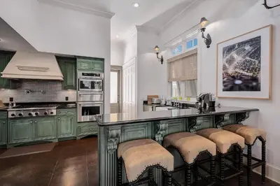 a kitchen with green cabinets and a bar with stools at Joben Cottage in Rosemary Beach