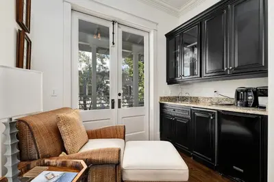 a living room with a chair and a kitchen with black cabinets at Joben Cottage in Rosemary Beach