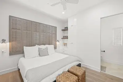 a white bedroom with a bed and a chair at Oasis Cottage & Carriage House in Rosemary Beach