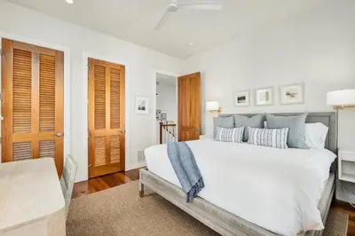 a white bedroom with a large white bed and wooden floors at R&B Cottage & Carriage House in Rosemary Beach