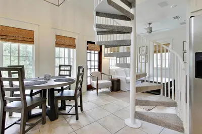 a dining room with a table and a spiral staircase at Southern Serenity Carriage House in Rosemary Beach