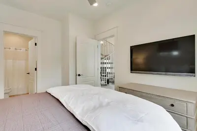 a white bedroom with a flat screen tv on the wall at Southern Serenity Carriage House in Rosemary Beach