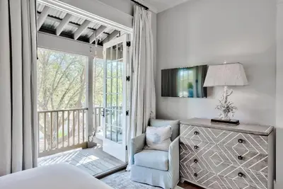 a bedroom with a bed and a chair and a window at Blue Heron Cottage & Carriage House in Rosemary Beach