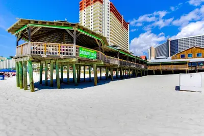 a wooden pier on the beach next to buildings at Steps to Sand and Surf! Family-Friendly PCB Retreat in Panama City Beach