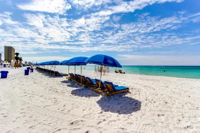 a row of blue umbrellas and chairs on a beach at Steps to Sand and Surf! Family-Friendly PCB Retreat in Panama City Beach