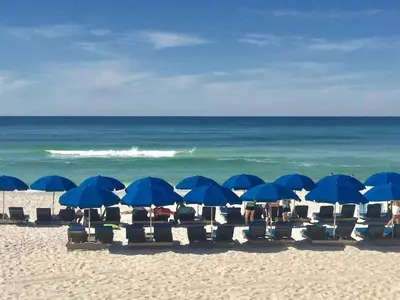 a group of chairs and blue umbrellas on a beach at Calypso 203 1 Bedroom Gulf Front in Panama City Beach