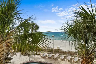 a view of the beach from a resort with chairs and palm trees at Calypso 203 1 Bedroom Gulf Front in Panama City Beach
