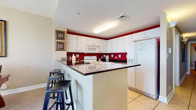 a kitchen with white cabinets and a counter with stools at Calypso I 407E in Panama City Beach