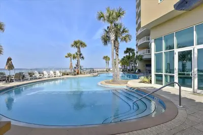a swimming pool with palm trees and a building at Aqua 511 in Panama City Beach