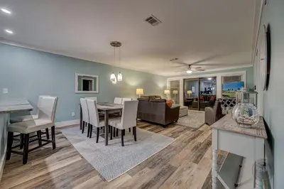 a dining room and living room with a table and chairs at Our Happy Place! Seasonal Beach SRV! Pool & Gulf Views! in Panama City Beach