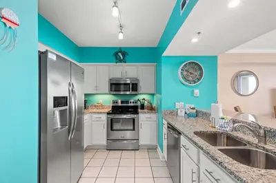 a kitchen with blue walls and stainless steel appliances at Emerald Beach Resort 234 | Roo’s Rendezvous in Panama City Beach