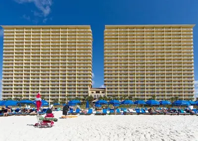 a beach with chairs and blue umbrellas and buildings at 1005 Calypso Direct Ocean Front Master on the Gulf in Panama City Beach
