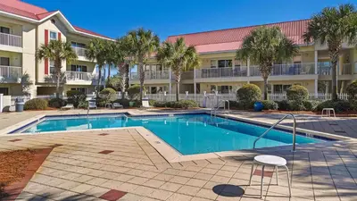 a swimming pool in front of a building with palm trees at Rollin Tides in Santa Rosa Beach