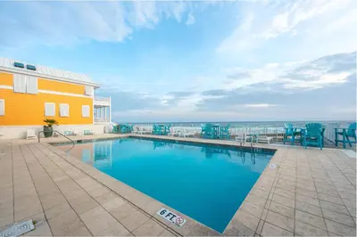 a swimming pool with blue chairs next to a yellow building at Grand Tortuga Crush in Panama City Beach