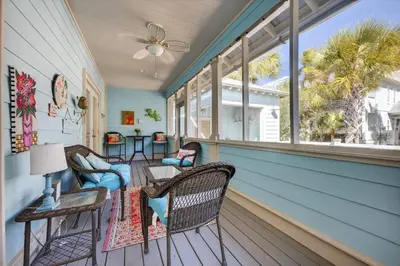 a porch with chairs and a table and windows at Cute as a Button in Inlet Beach