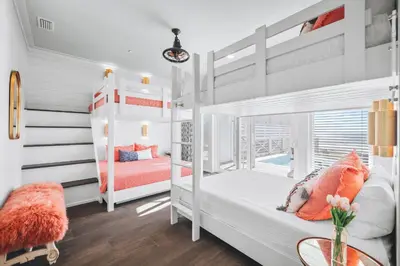 a white bedroom with two bunk beds and a table at The Sand Castle by 30A Escapes in Panama City Beach