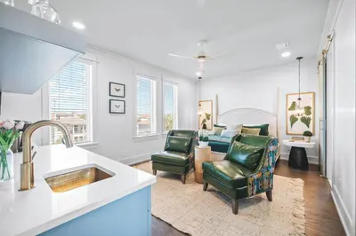 a kitchen with two green chairs and a living room at The Sand Castle by 30A Escapes in Panama City Beach