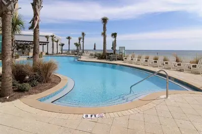 a swimming pool with palm trees and the ocean at Aqua 408 in Panama City Beach
