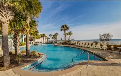 a swimming pool with palm trees and the ocean at Aqua 410 in Panama City Beach