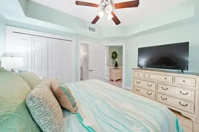 a bedroom with a bed with a ceiling fan and a flat screen tv at Calypso 803W in Panama City Beach