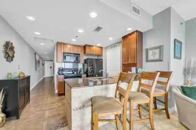 a kitchen with wooden cabinets and a bar with chairs at Sterling Breeze 1903 in Panama City Beach