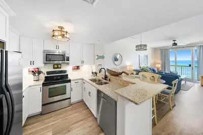 a kitchen with white cabinets and appliances and a living room at Calypso 908W Stunning condo, beach front, and immaculate in Panama City Beach