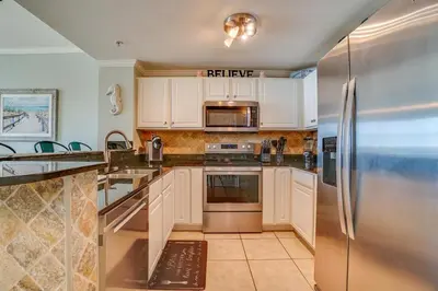 a kitchen with white cabinets and a stainless steel refrigerator at Calypso 202E Paradise at Calypso 4 chairs daily Gulf Front in Panama City Beach