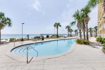 a swimming pool with palm trees and the ocean at Calypso 202E Paradise at Calypso 4 chairs daily Gulf Front in Panama City Beach