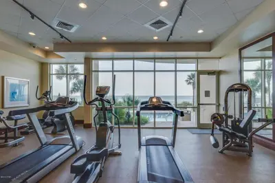 a gym with treadmills and ellipticals in a room with windows at Aqua 1710 in Panama City Beach
