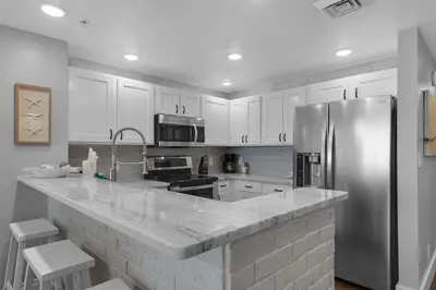 a kitchen with white cabinets and a stainless steel refrigerator at Calypso 302 West Direct Beach Front Awesome! in Panama City Beach