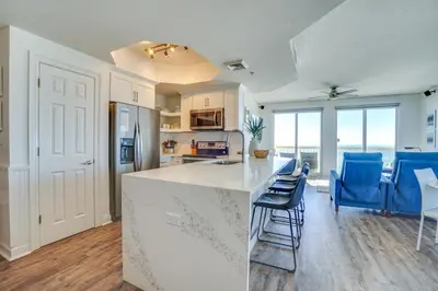 a kitchen and living room with a counter and blue chairs at Calypso 909 West Tower GULF FRONT 3BR 3BA Views Forever in Panama City Beach