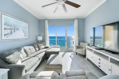 a living room with a sectional couch and a television at Calypso 2306W Penthouse VIP Parking and 2 sets of beach chairs in Panama City Beach